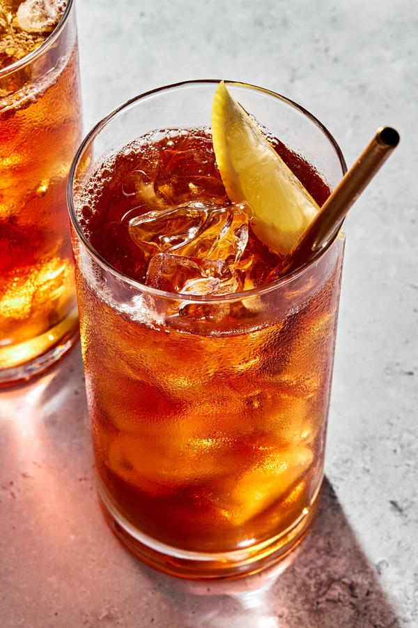 a glass of homemade iced tea with a metal straw sweetened with sugar and garnished with a lemon wedge