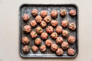 raw pork meatballs rolled on a baking sheet