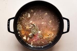 pasta being added to italian meatball soup in a black soup pot