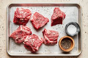 raw roast cut into 3 inch chunks being seasoned with salt and pepper