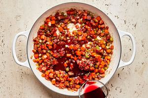 red wine being poured into a pot with pancetta, onion, carrots, and celery