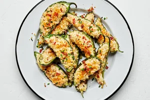 Plate of homemade jalapeño poppers stuffed with creamy cheese filling and bacon with a crispy golden breading.