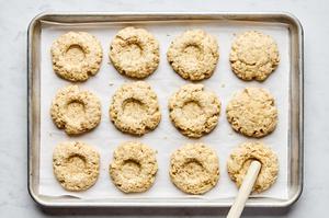 wells being made with a wooden spoon in partially baked oat scones on a parchment lined baking sheet