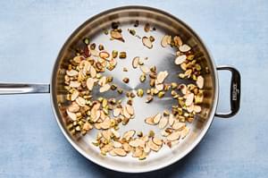 pistachios and slices almonds being toasted in a skillet