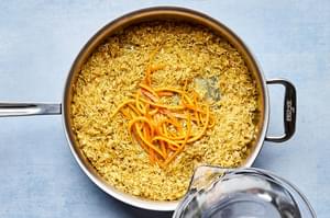 water being poured into a pan with rice, spices and orange zest