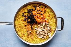 a pot of rice with pistachios, almonds and dried fruit being stirred in