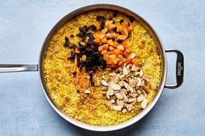 a pot of rice with pistachios, almonds and dried fruit being stirred in