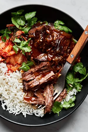 korean style pot roast in a bowl served with white rice and kimchi and topped with cilantro