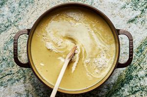 wooden spoons stirring heavy cream into leek soup in a large cast iron dutch oven.