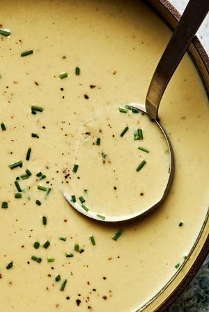 close up of leek soup topped with chives being scooped out of a pot with a ladle.