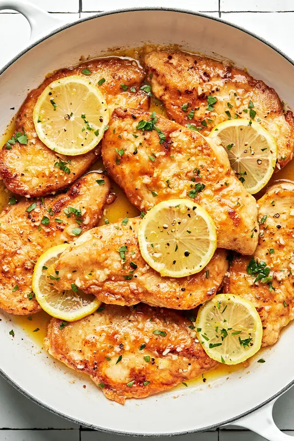 lemon butter chicken in a pan topped with fresh lemon slices and sprinkled with fresh parsley