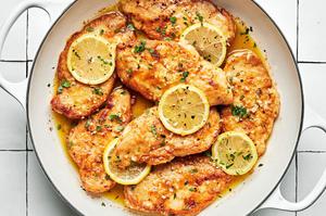 lemon butter chicken in a pan topped with fresh lemon slices and sprinkled with fresh parsley