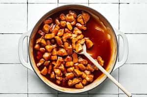 lemon teriyaki chicken being stirred with a wooden spoon in a skillet