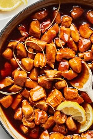 lemon teriyaki chicken being stirred with a wooden spoon in a skillet
