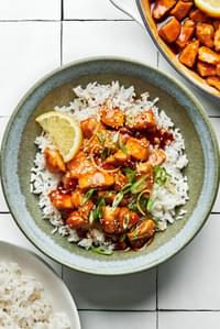 lemon teriyaki chicken in a bowl served over white rice and sprinkled with sesame seeds and sliced green onions