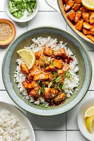 lemon teriyaki chicken in a bowl served over white rice and sprinkled with sesame seeds and sliced green onions