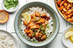 lemon teriyaki chicken in a bowl served over white rice and sprinkled with sesame seeds and sliced green onions