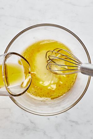 lemon juice, dijon mustard, sugar, salt, olive oil and chives being whisked together in a bowl to make lemon vinaigrette