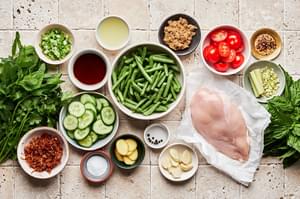 raw chicken breast, green beans, cucumbers, tomatoes, lemongrass, mint, basil, garlic, and fried shallots in prep bowls