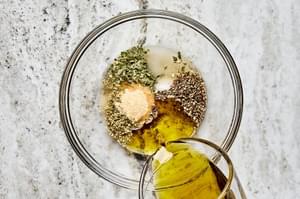 salt, garlic powder, oregano, basil, pepper, olive oil, vinegar, and sugar being combined in a glass bowl to make dressing
