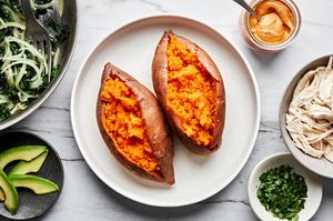 baked sweet potatoes surrounded by toppings: sauteed kale and onions, chicken, avocado & chipotle cashew cream sauce