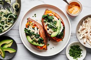 baked sweet potatoes being loaded with kale, onions, chicken, avocado, cilantro & chipotle cashew cream sauce