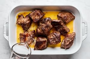orange juice, lime juice and tequila being poured in a baking dish with browned beef