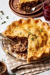 A homemade meat pie being sliced, revealing its savory filling of meat and seasoning inside a golden, flaky crust.