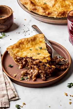 A slice of homemade meat pie with savory meat and potato filling inside a golden, flaky crust.