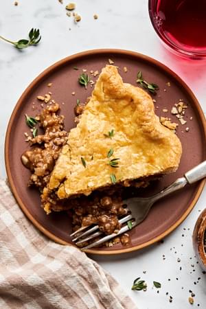 A slice of homemade meat pie with savory meat and potato filling inside a golden, flaky crust.