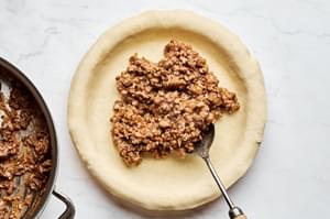 A meat pie being filled and assembled, with seasoned meat placed into a flaky crust, ready to be topped and baked.