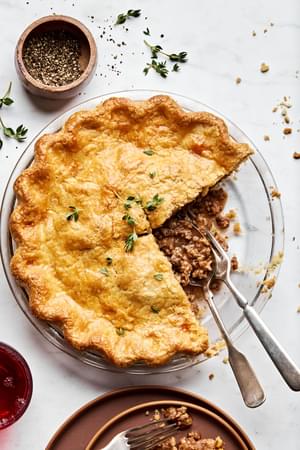 A homemade meat pie being sliced, revealing its savory filling of meat and seasoning inside a golden, flaky crust.