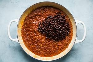 black beans being added to chicken stock, brown rice, taco seasoning tomato sauce in a pot