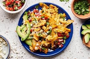 a plate of migas topped with pico de gallo, avocado, cilantro and cotija