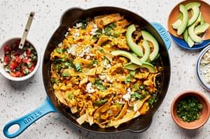 migas in a skillet topped with pico de gallo, avocado, cilantro and cotija