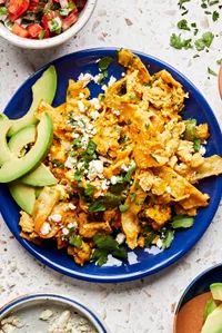a plate of migas topped with pico de gallo, avocado, cilantro and cotija