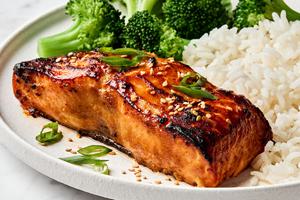 miso glazed salmon topped with green onions and sesame seeds served on a plate with white rice and steamed broccoli