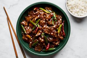 a bowl of homemade mongolian beef next to a bowl of white rice and chop sticks