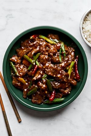 a bowl of homemade mongolian beef next to a bowl of white rice and chop sticks