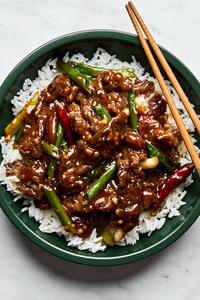 a bowl of homemade mongolian beef served on top of white rice with chop sticks