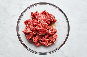 thinly sliced flank steak being tossed with Shaoxing wine and soy sauce in a bowl