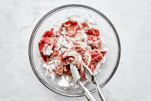 corn starch being added to a bowl of thinly sliced flank steak tossed with Shaoxing wine and soy sauce in a bowl