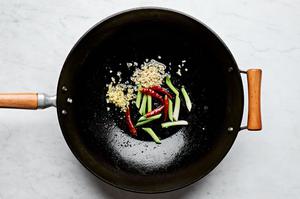 ginger, garlic, white parts of the green onions, and peppers being cooked in a wok