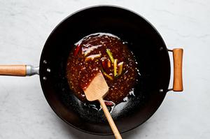 mongolian sauce being added to ginger, garlic, green onions, and peppers in a wok