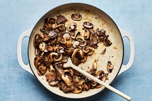 mushrooms in olive oil and salt being cooked in a skillet with a wooden spoon
