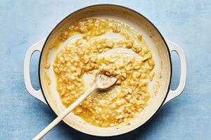 shallots, garlic, butter and flour being cooked together in a skillet being stirred with a wooden spoon
