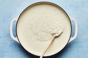 homemade sauce for mushroom lasagna being stirred in a pot with a wooden spoon made with Parmesan and crème fraîche