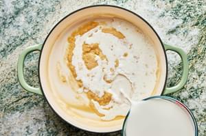 milk being poured into a braiser with butter and flour