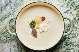 crème fraîche, dijon, garlic powder, nutmeg, thyme, salt, and pepper being added to cream sauce in a braiser