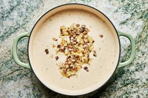 cheese, cooked onions and mushroom stems being added to cream sauce in a braiser